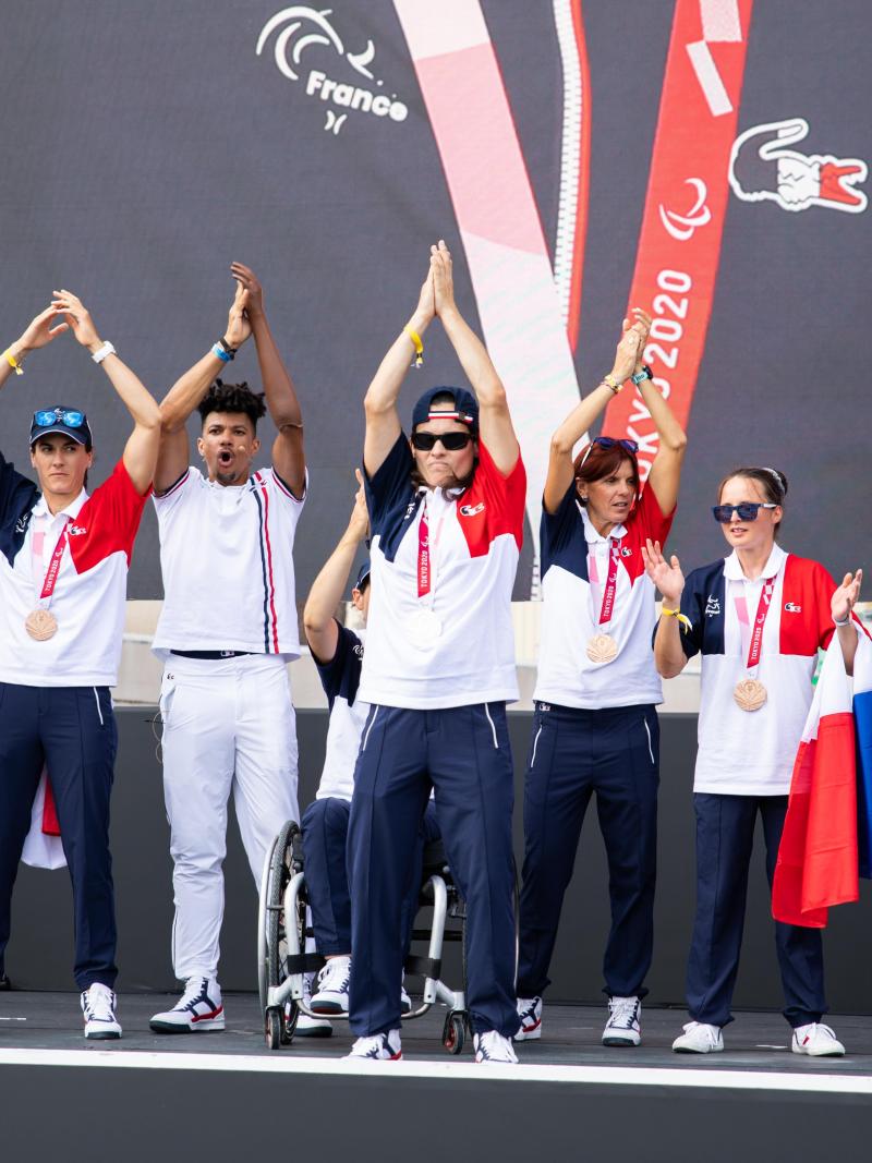 Ten people in French uniforms clap onstage with their hands raised high.