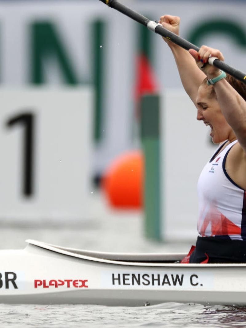 A female Para canoeist raises her paddle and yells out in celebration after crossing the finish line.