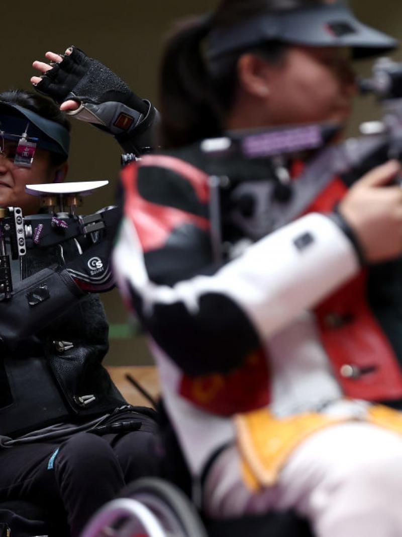 A female rifle shooter behind another shooter waving at at shooting range