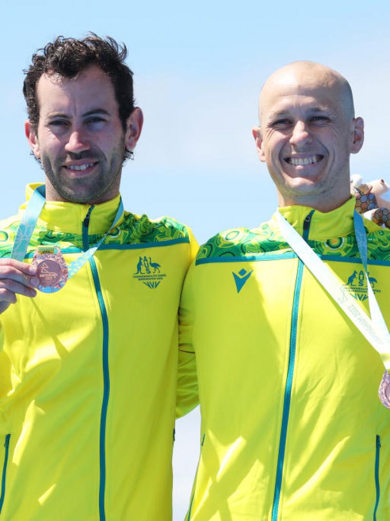 Para triathlete and his guide each hold a bronze medal and smile