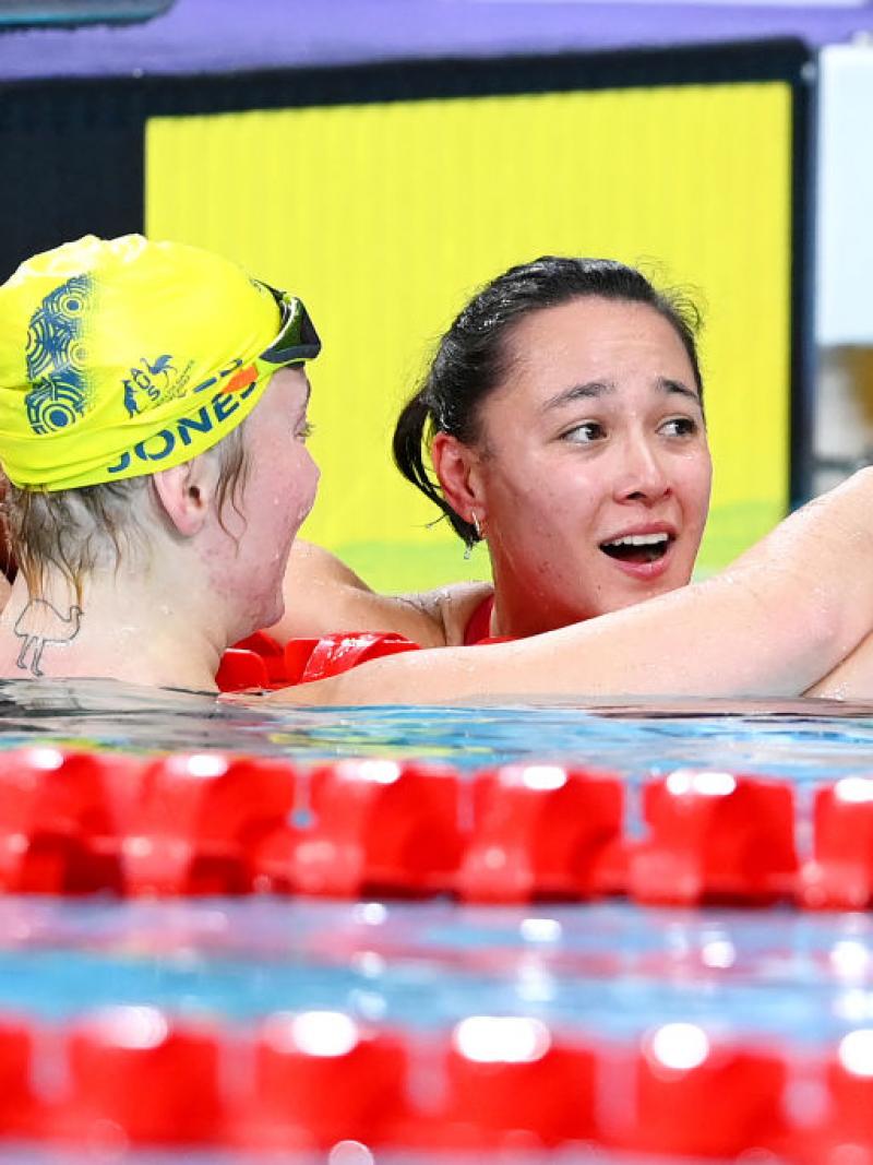 A female swimmer embracing another female swimmer looking surprised in the pool