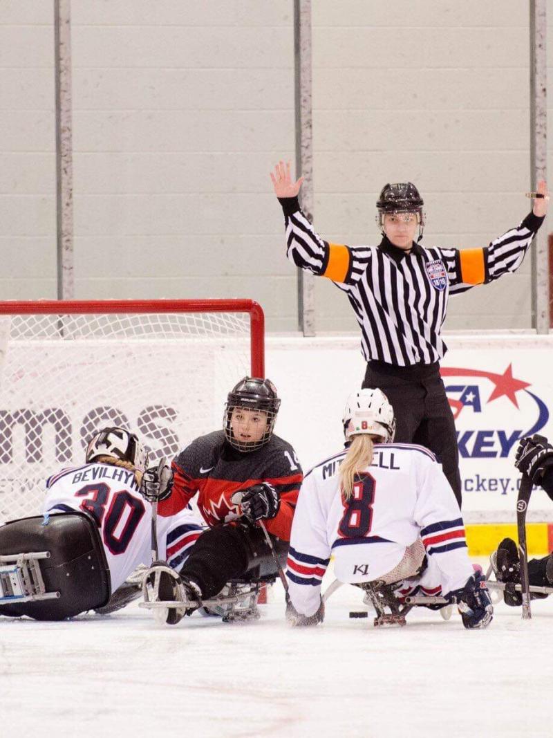 A female Para ice hockey official raising her arms in front of five female players