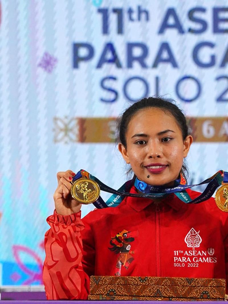 A woman showing her gold medals with a backdrop of the 11th ASEAN Para Games