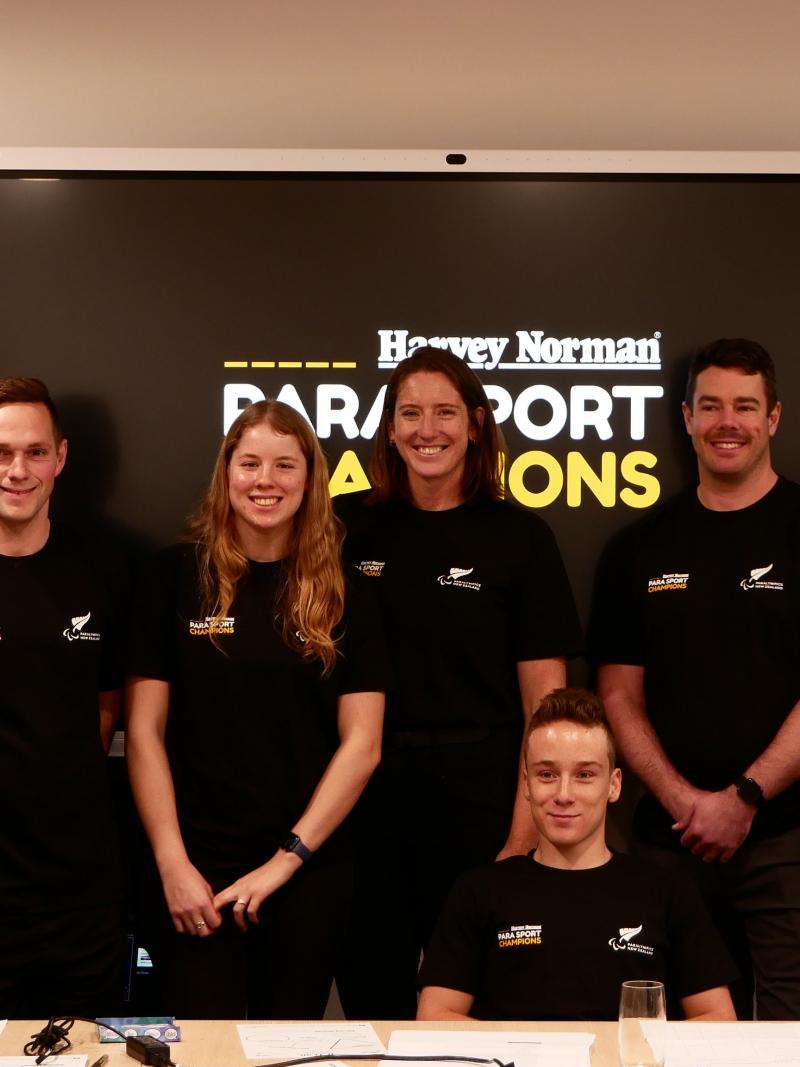 Seven Para athletes pose for a photograph in front of a screen and posters with the words "Harvey Norman Para Sport Champions."