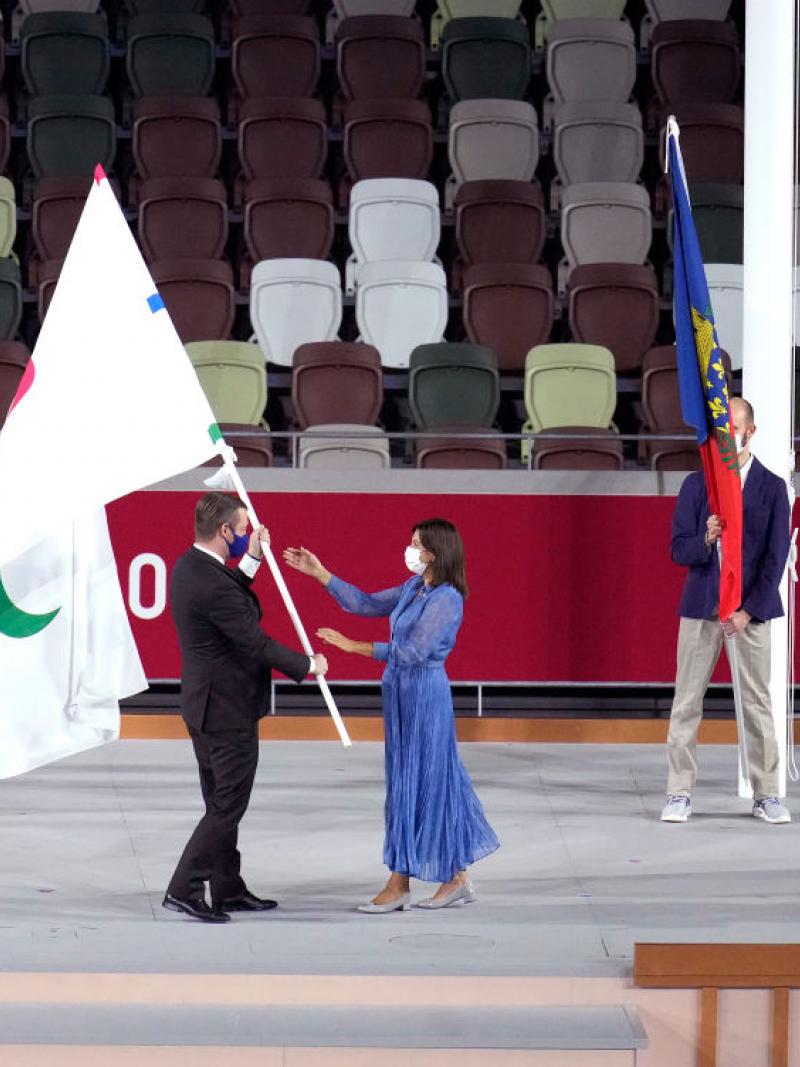 A man passes the Paralympic flag to a woman who stretches out her hands to receive it.