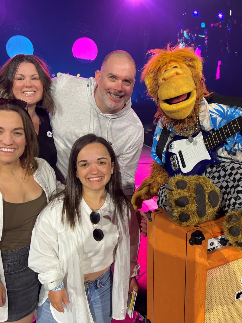 Two swimmers, a coach and manager pose with a puppet from the fictional band The Weirdos.
