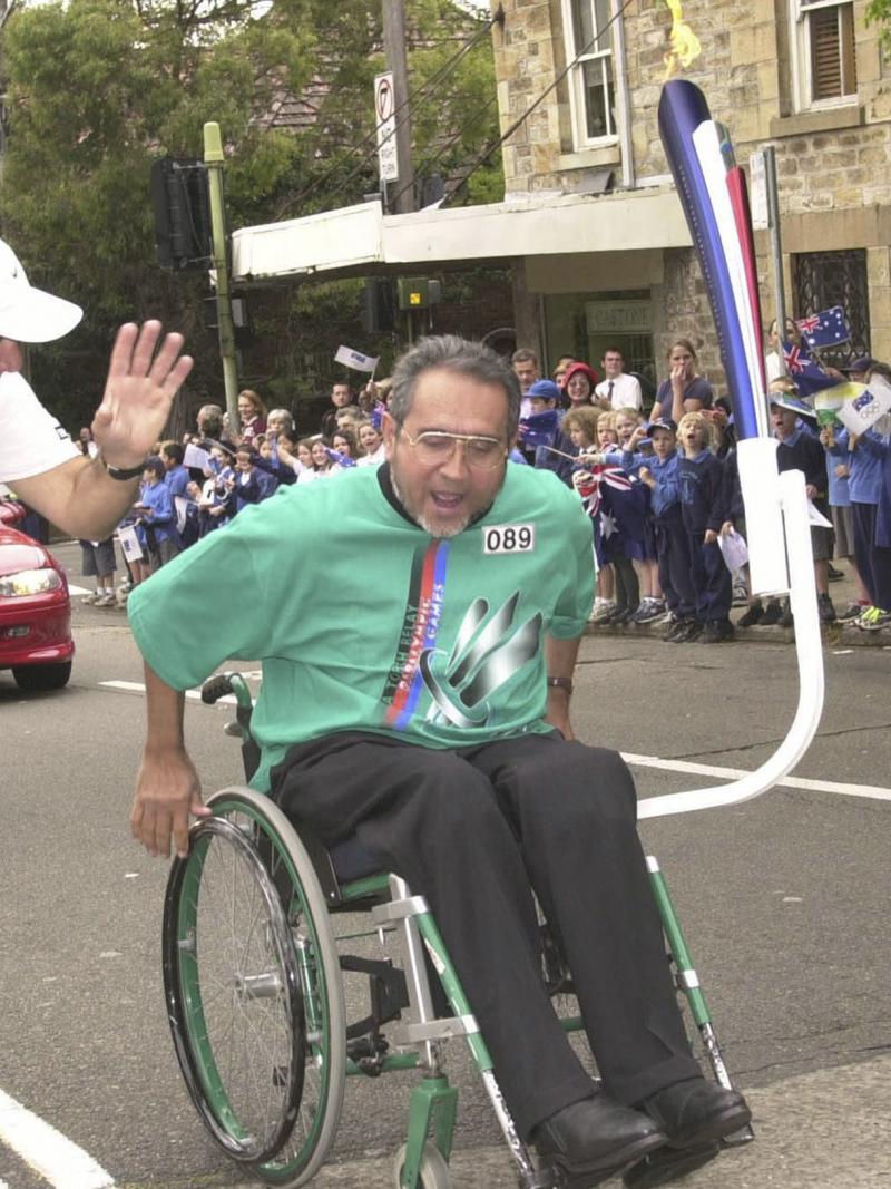 A man pushes his wheelchair in front of a crowd of young spectators as part of the Sydney 2000 torch relay.