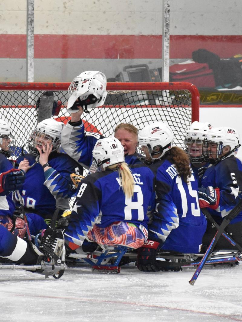 Female Para ice hockey players on sleds celebrate in a circle.