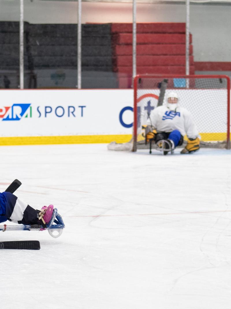 A woman in green jersey and on a sled is preparing herself to shoot the puck.