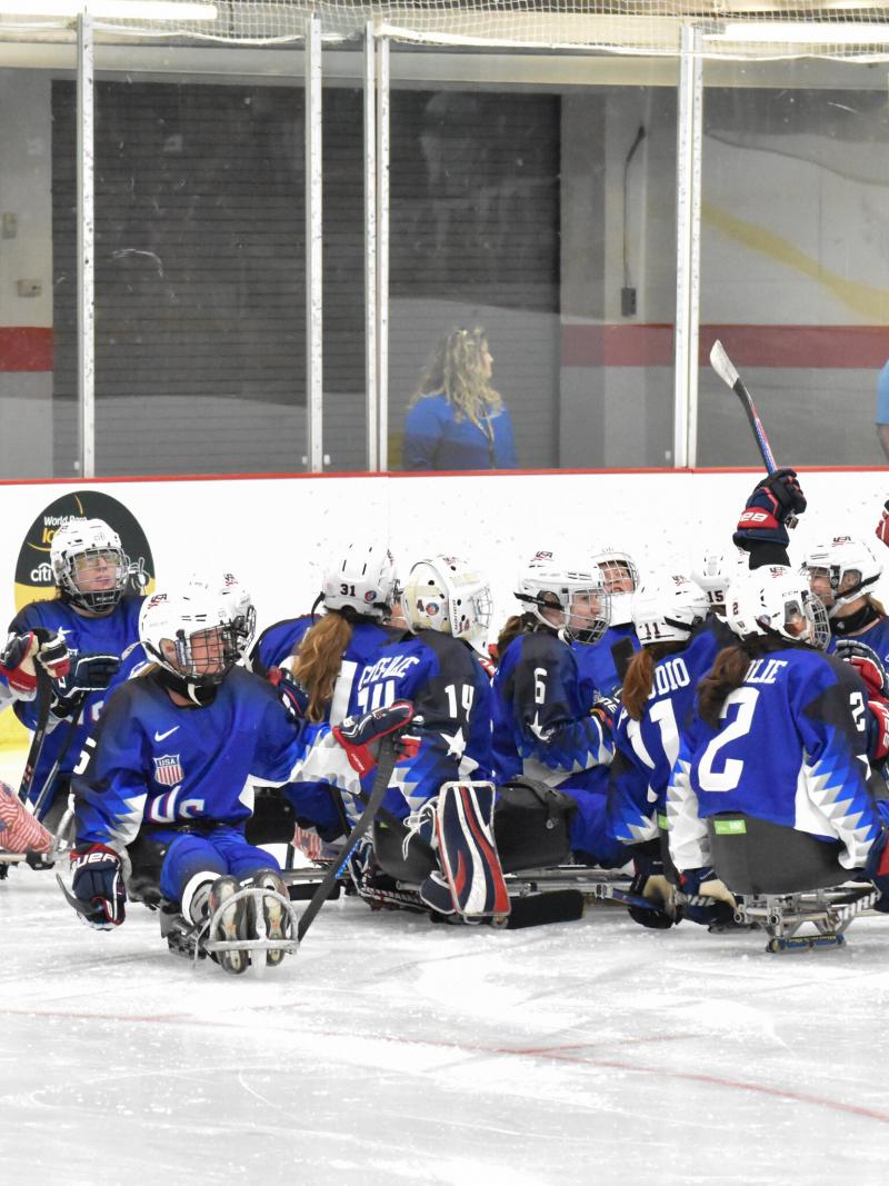 Female Para ice hockey players in blue jerseys celebrate on ice