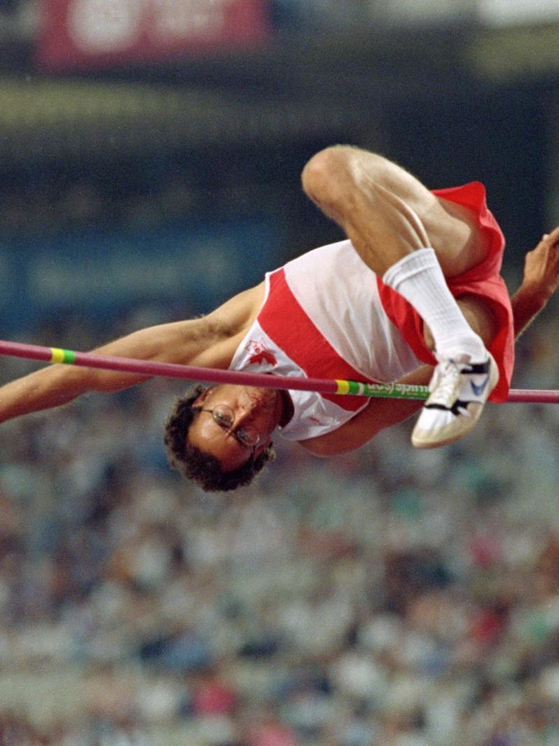 A male athlete jumps over the bar in a stadium full of spectators.