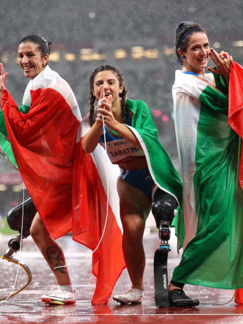 Three female athletes pose by raising two fingers in front of their faces at the Tokyo 2020 Paralympic Games.