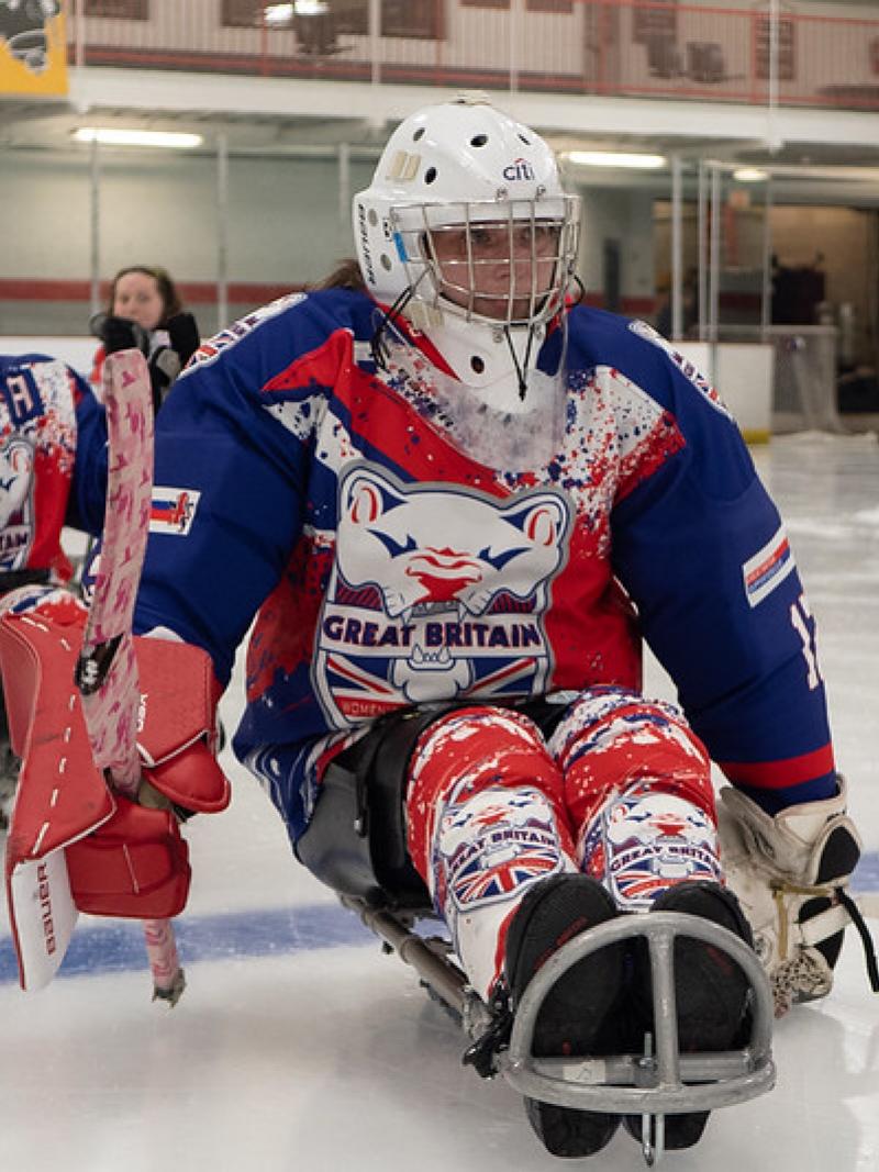 Female Para ice hockey players wearing Great Britain jerseys form a line on the rink.
