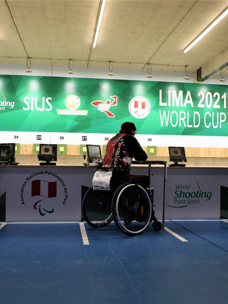 Three shooters in wheelchairs competing in an indoor shooting range