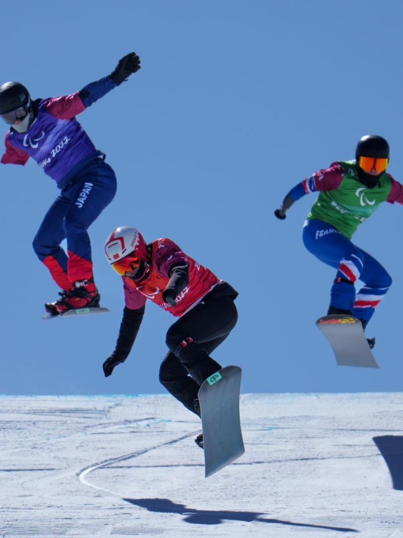Three male Para snowboarders jump during the snowboard cross race at Beijing 2022.