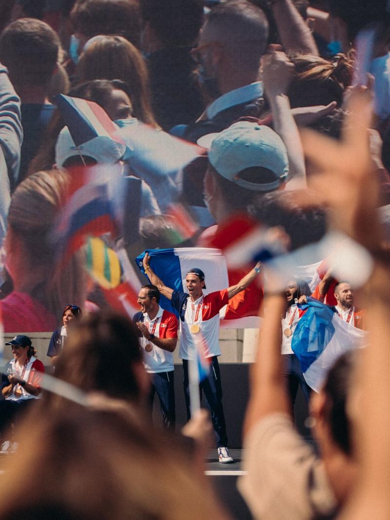 Athletes raise and wave French flags on stage as audience members clap.