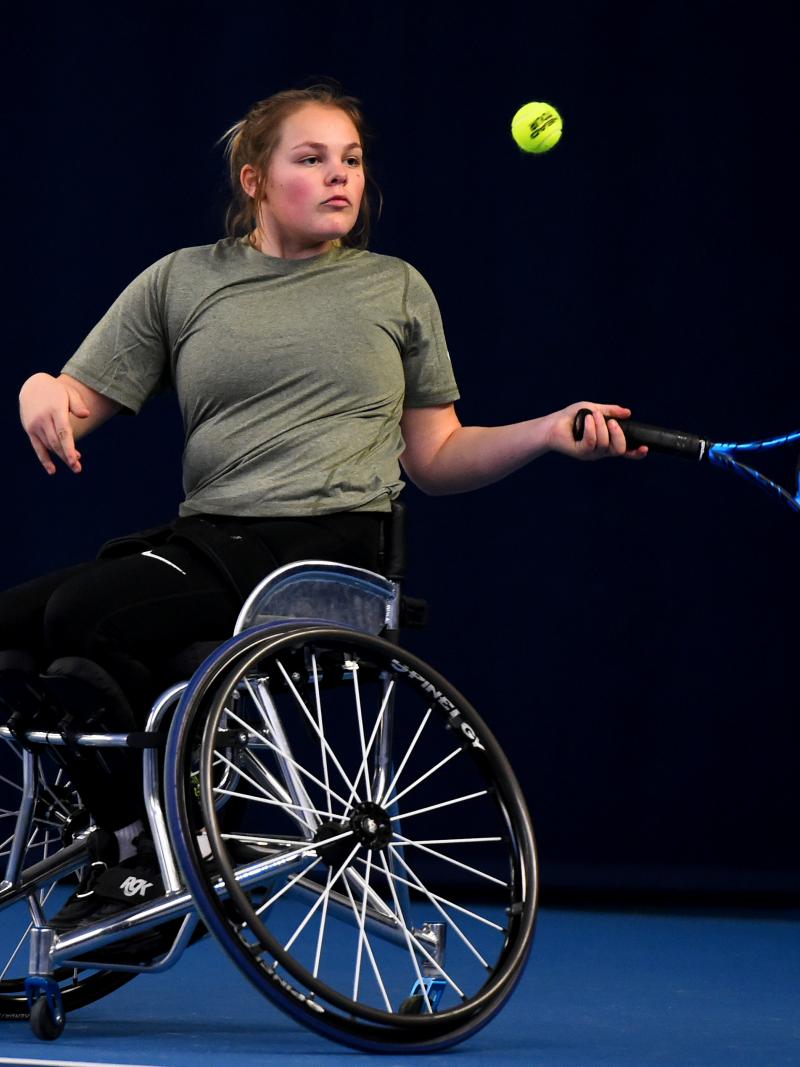 A female wheelchair athlete plays a forehand on a blue court.