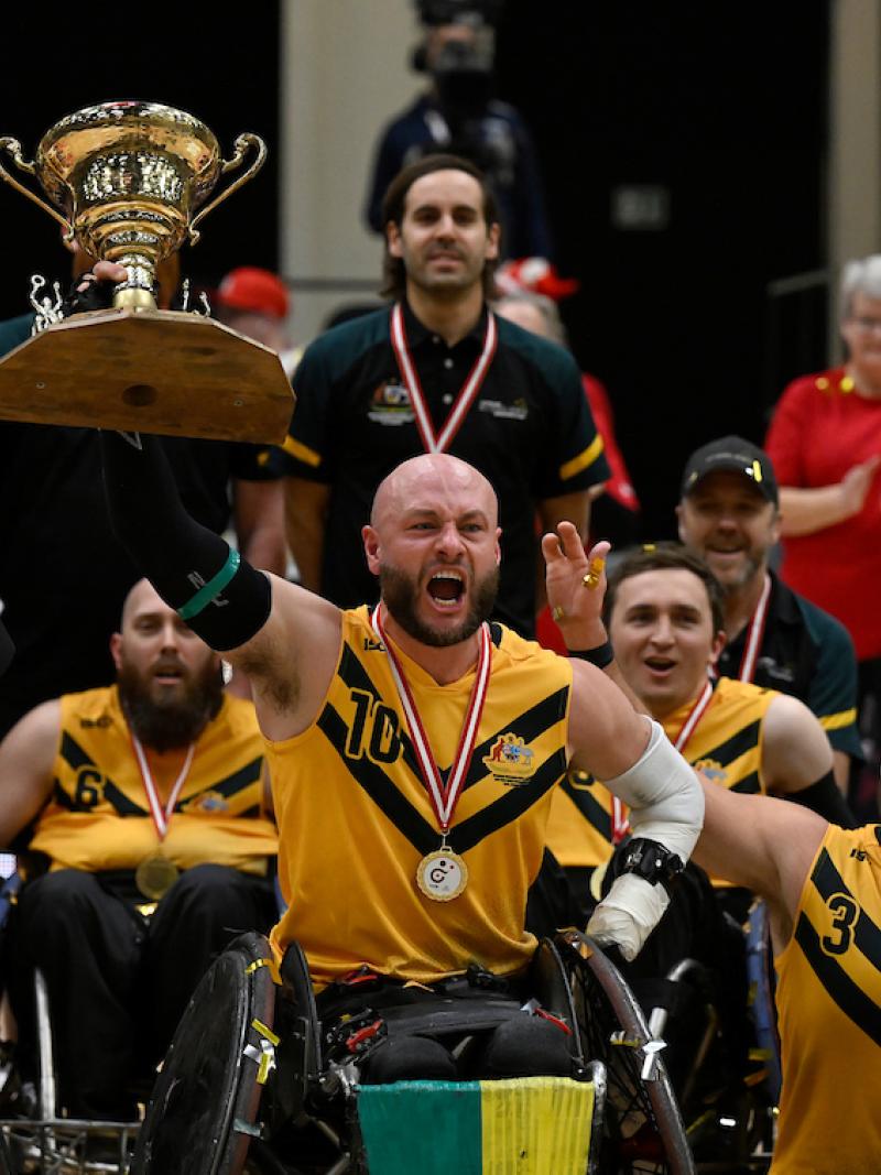 Wheelchair rugby players wearing yellow jerseys celebrate their victory
