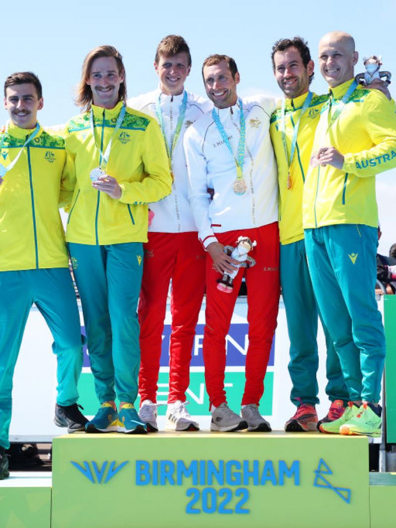 Six male athletes stand on the podium