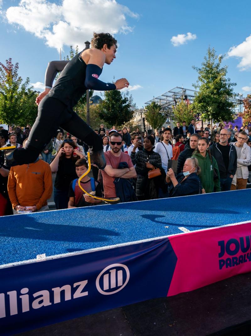 A male long jumper on two blades runs along a blue track towards a sandpit.