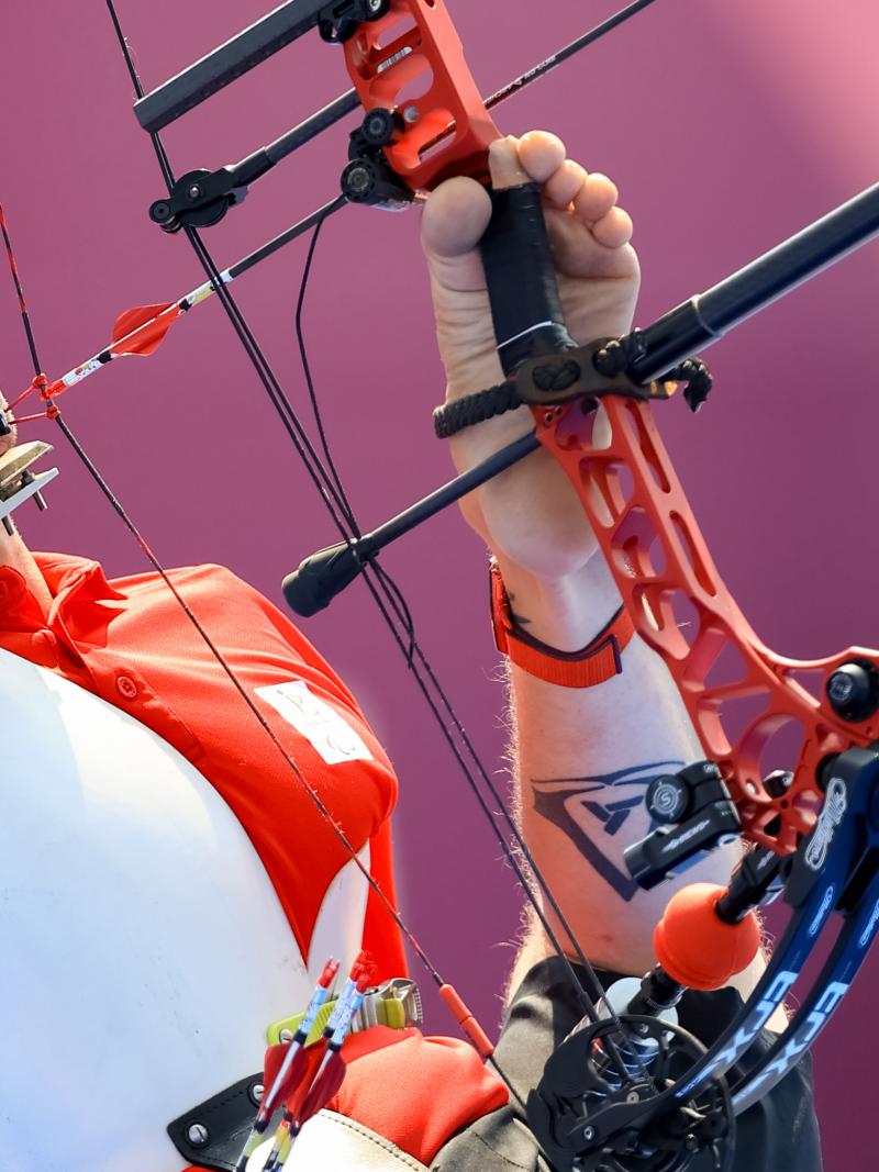 A man holds the bow with his legs and prepares to draw the arrow with his mouth.