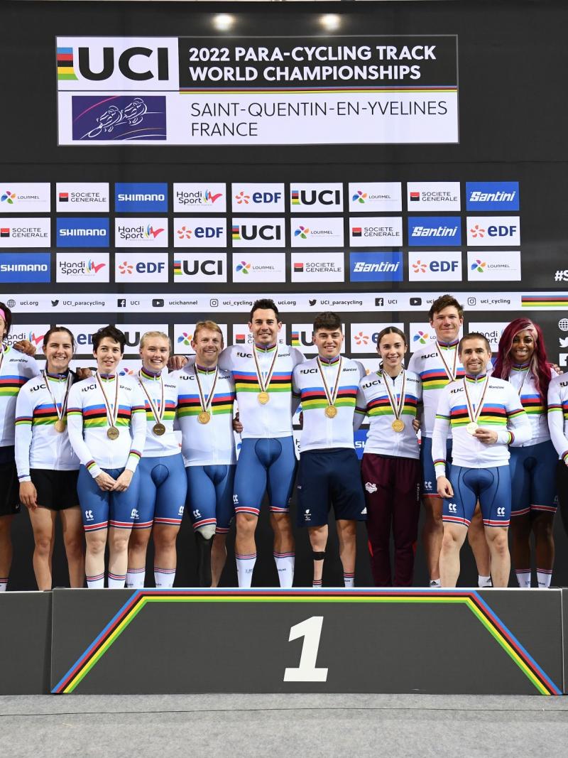 Fourteen British Para cyclists, all with medals, pose for a group picture on the podium.
