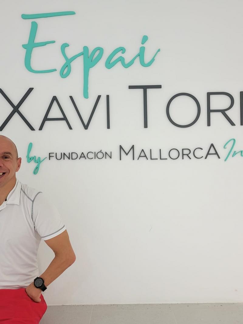 A male athlete smiles in front of the wall with the words "Espai Xavi Torres by Fundacion Mallorca Integra"