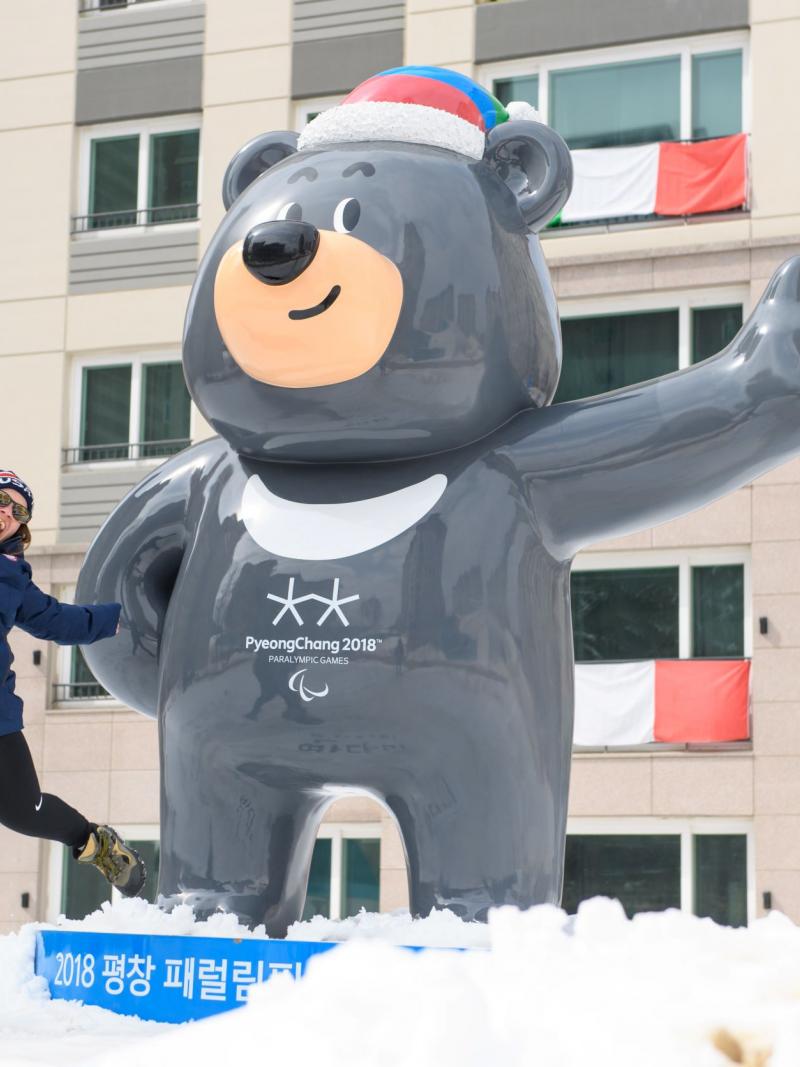 A woman jumps next to a mascot of the Pyeongchang 2018 Paralympic Games