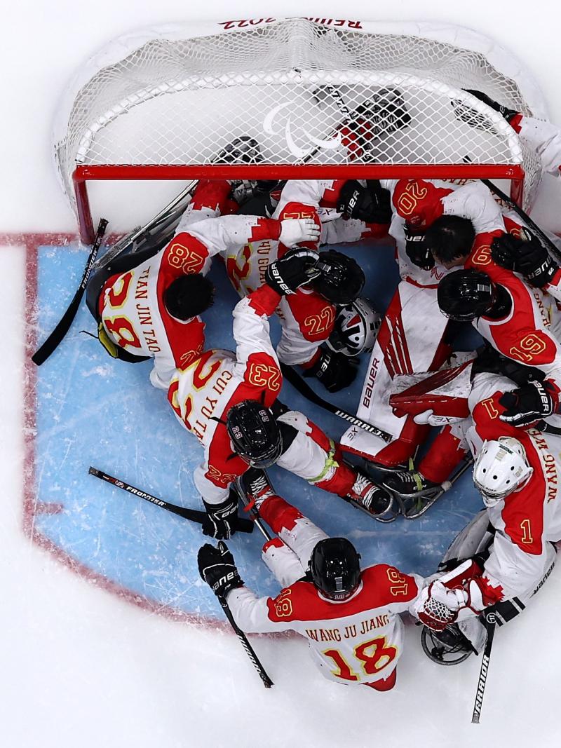 An aerial view of a Para ice hockey team celebrating in front of the goal on an ice rink