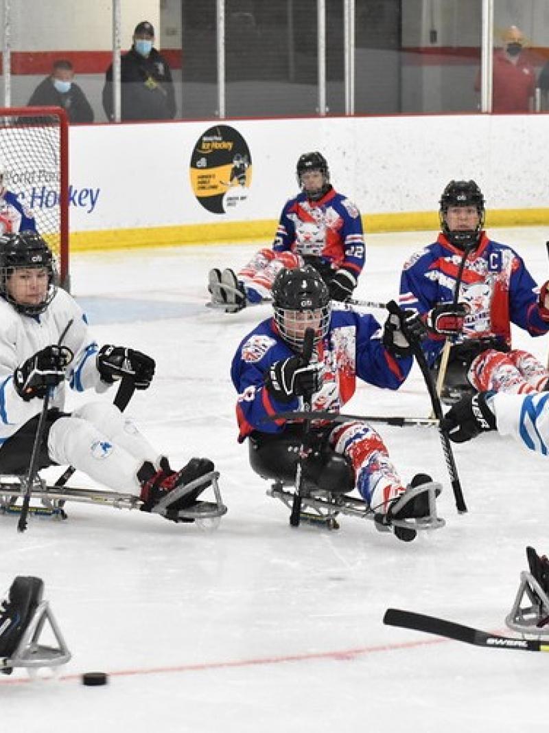 Seven female Para ice hockey players on ice in front of a goalie