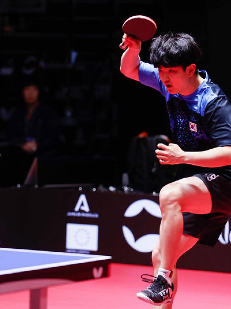 A male table tennis player jumps backward with a table tennis racket in his right hand