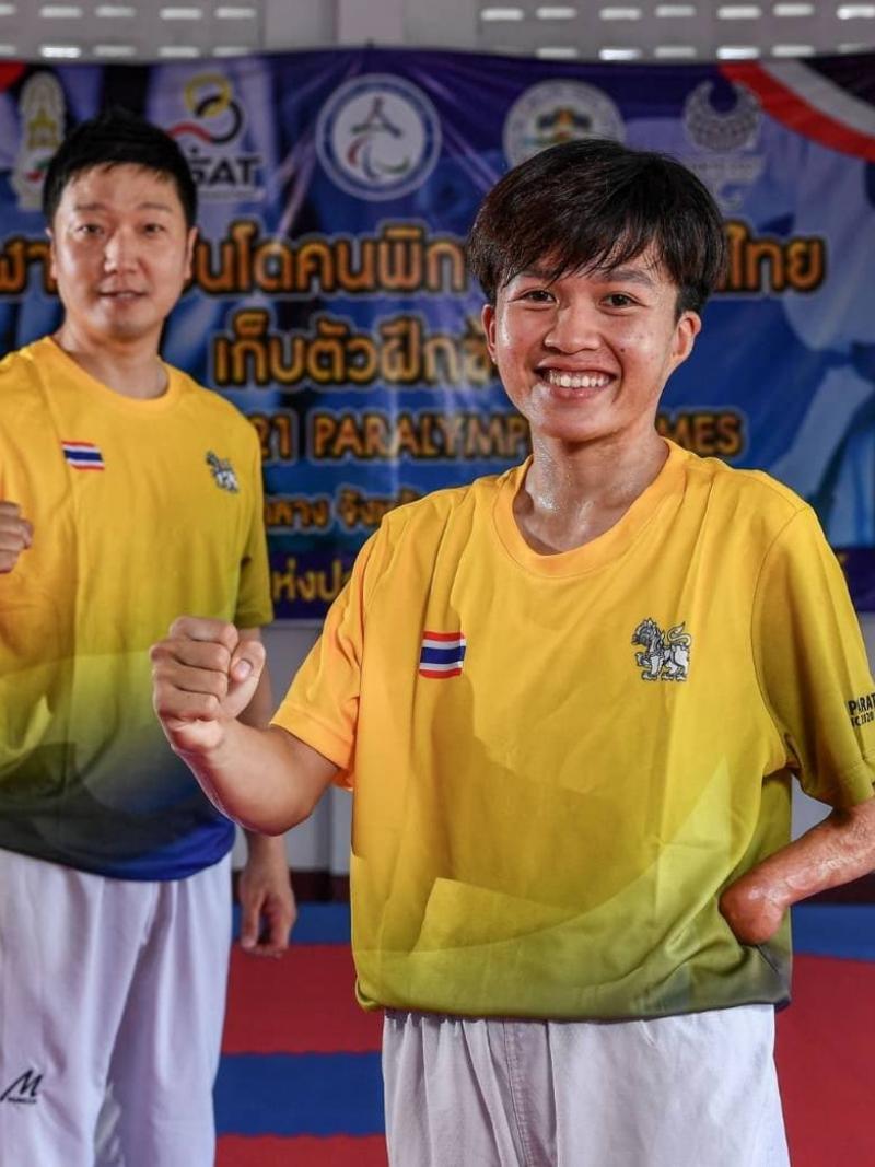 A woman with a left arm missing near the wrist and a man pump their right fists while standing on a training mat.