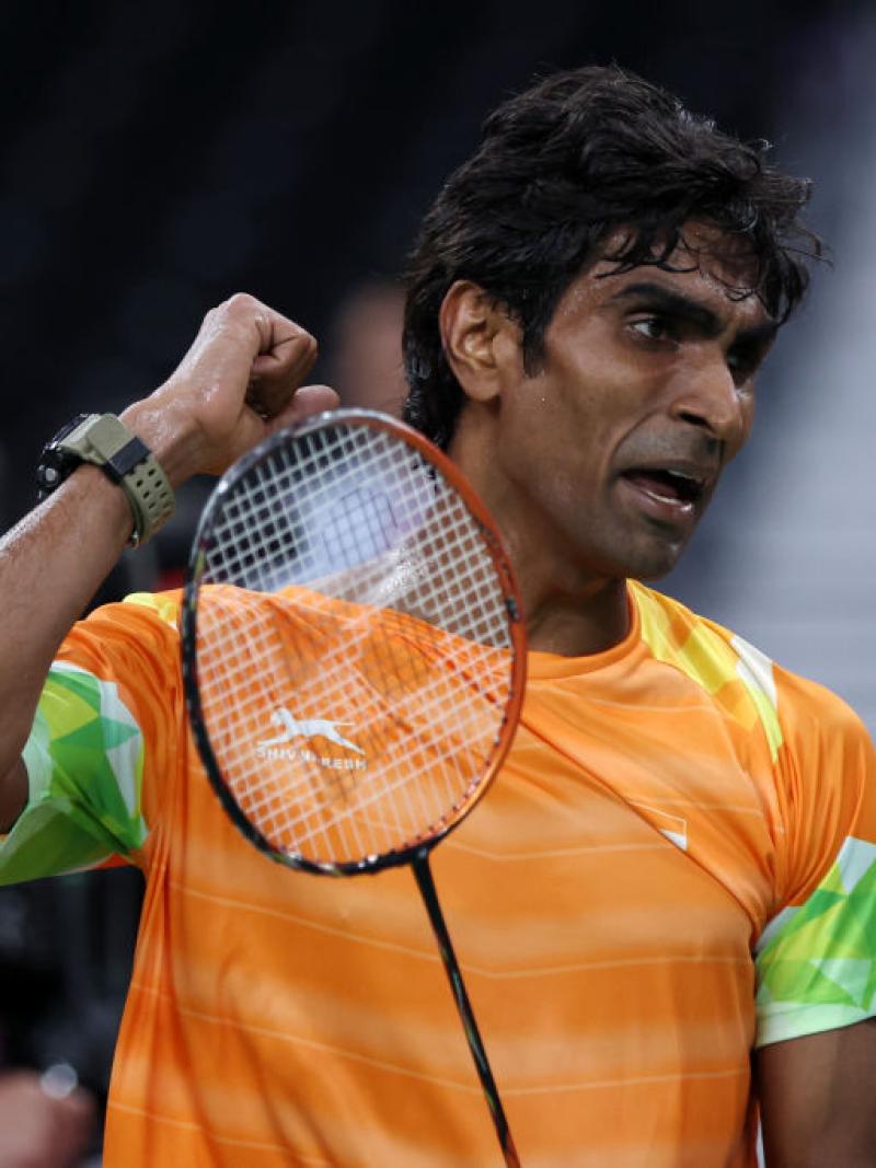 A male athlete pumps his right fist, while holding a badminton racket with the other hand