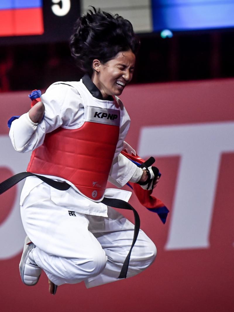 A female Para taekwondo athlete jumps with joy while holding a Nepalese flag after winning the final fight.