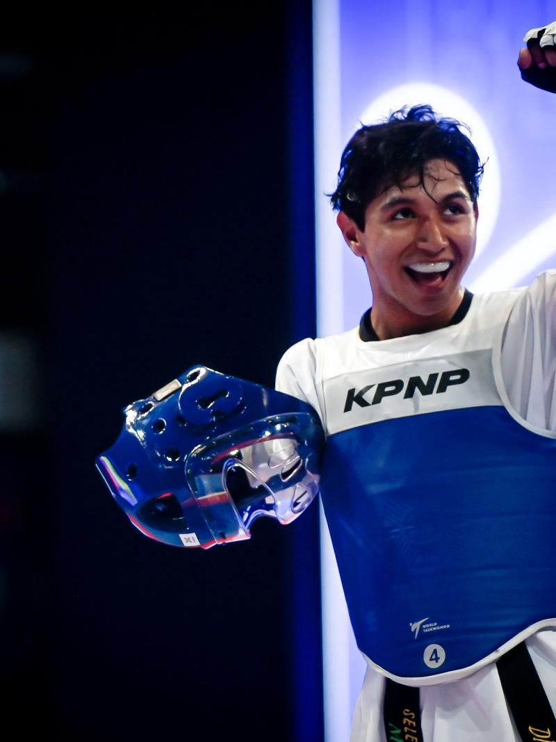 A male Para taekwondo athlete pumps his fist with his helmet off.