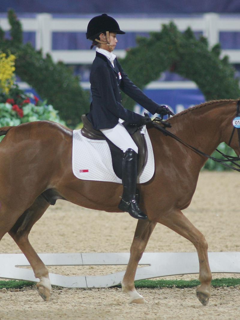 A female athlete rides a horse, walking calmly, during competition.
