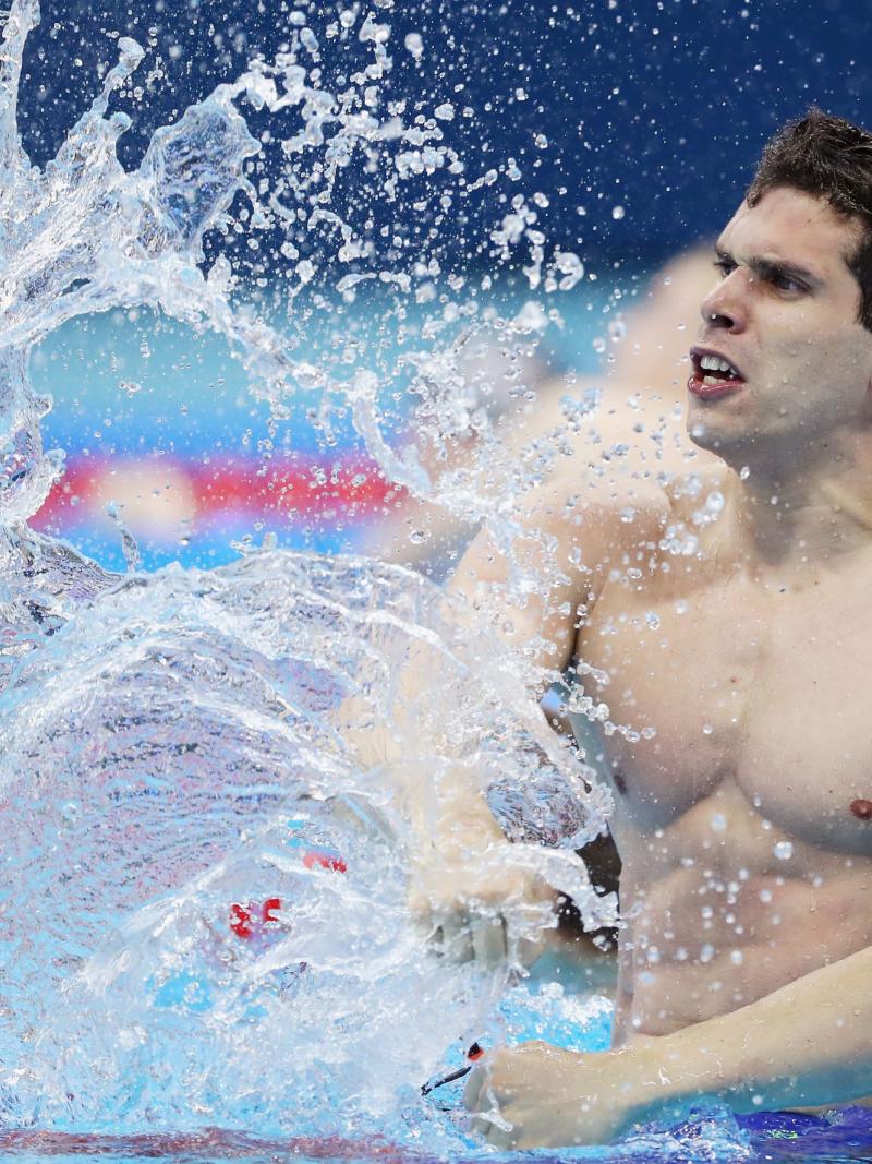 A male swimmer creates a big splash as he hits the water with his right fist after the finish of the race.