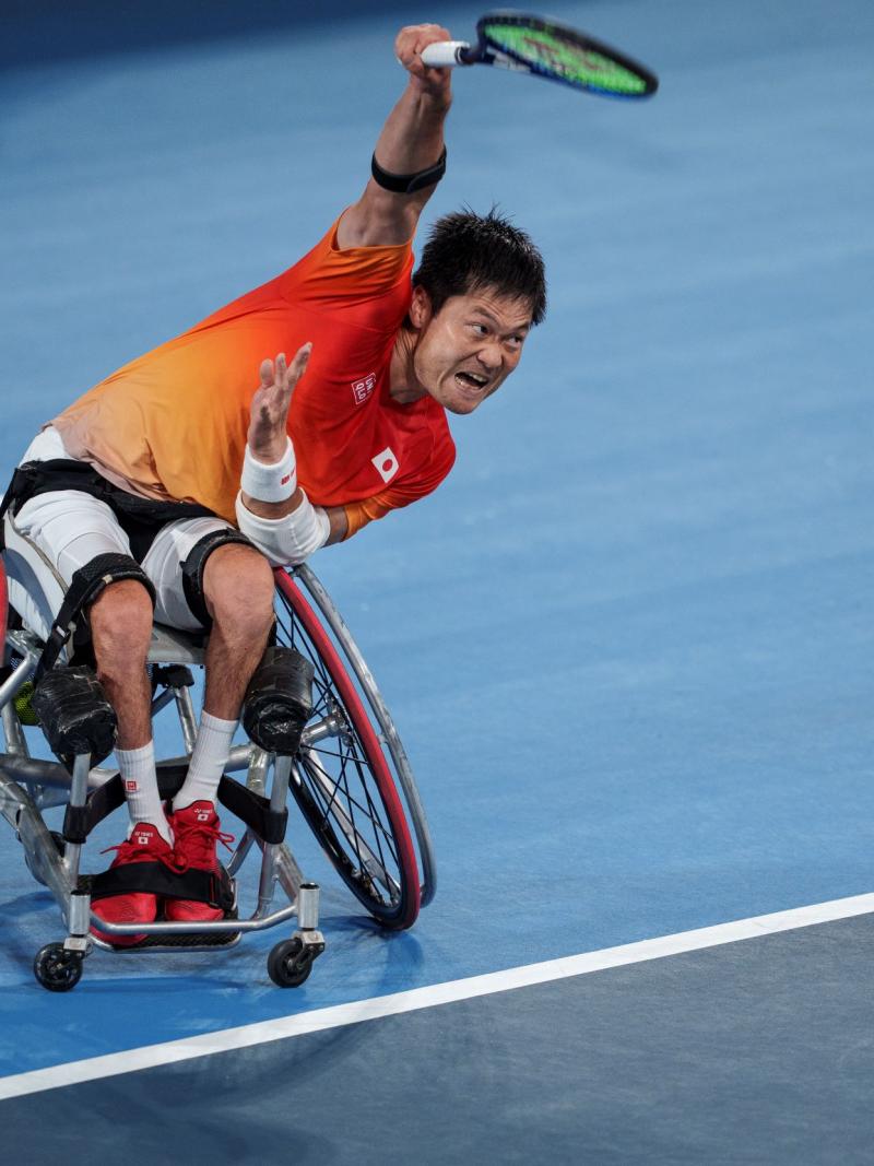 A male wheelchair tennis player holds the tennis racquet with his right hand
