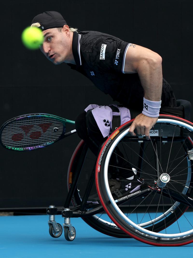 A male wheelchair tennis player eyes the ball with focus as he prepares to return it during a match.