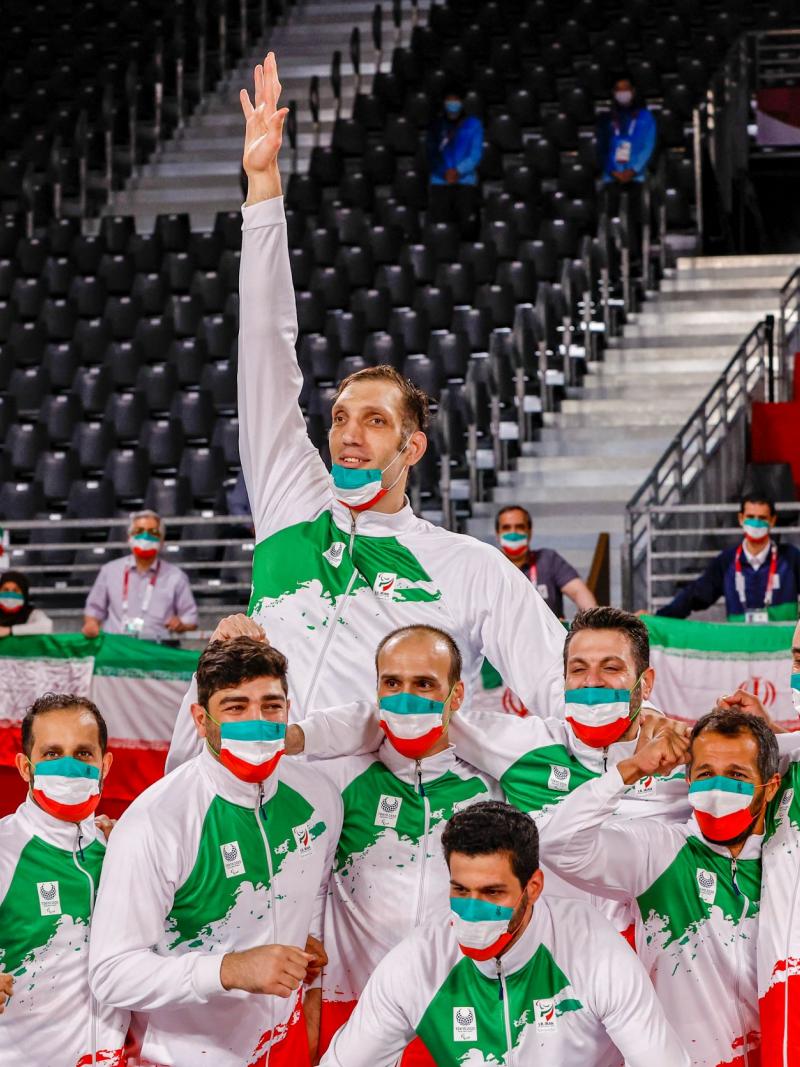 Male sitting volleyball athletes in national uniforms and masks featuring the Iranian flag pose for a photo as they wait for the medal ceremony at Tokyo 2020.