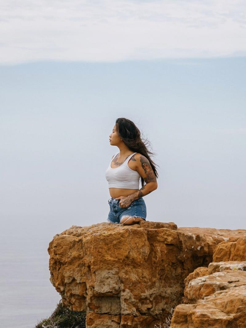 A young female without legs below the hips stands on a cliff looking out a large body of water.