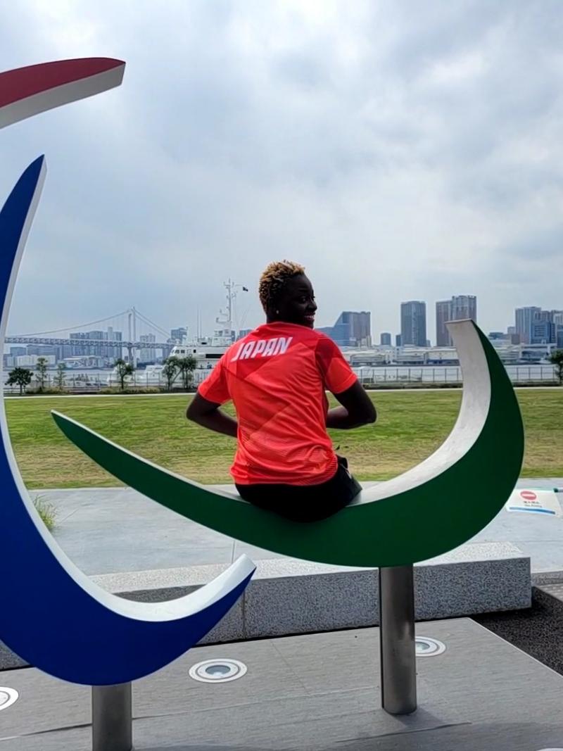 A female athlete wearing Japan's red uniform sits on the Three Agitos monument.