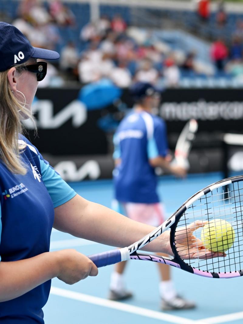 A female athlete prepares to serve a yellow ball used in blind and low vision tennis