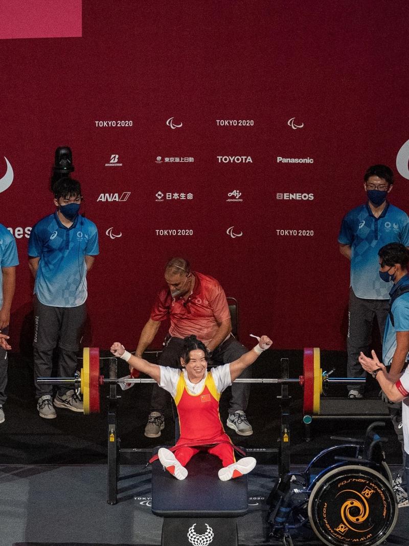 A female Para powerlifter celebrated on stage with five people around her