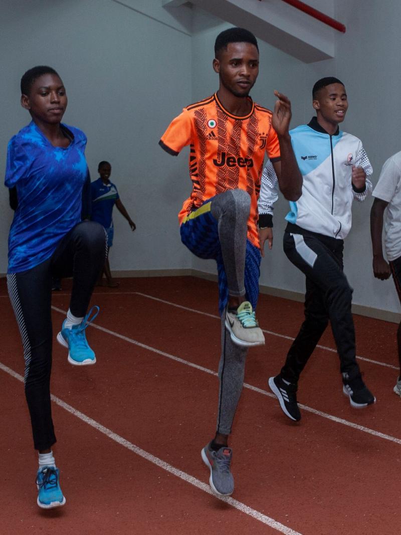 Five African athletes train, doing upward kicks, on an indoor track.