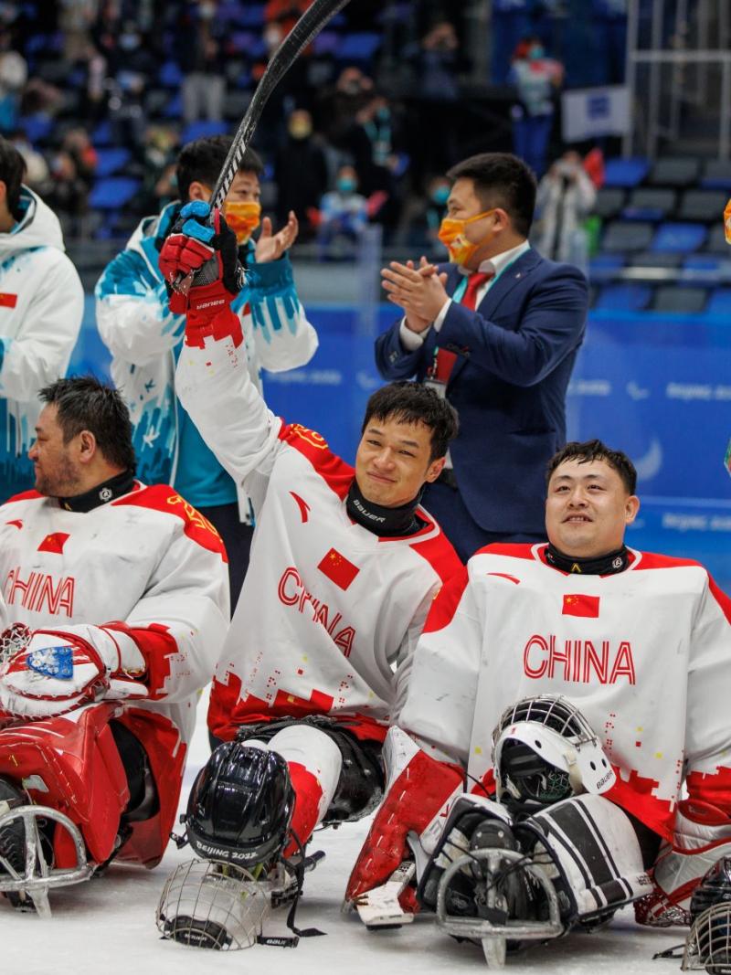 Five male athletes wearing China's red and white jersey celebrate on the rink, while four officials stand behind them clapping their hands