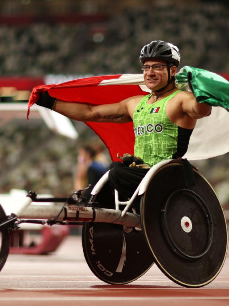 A male wheelchair racer with the Mexican flag at an athletics track