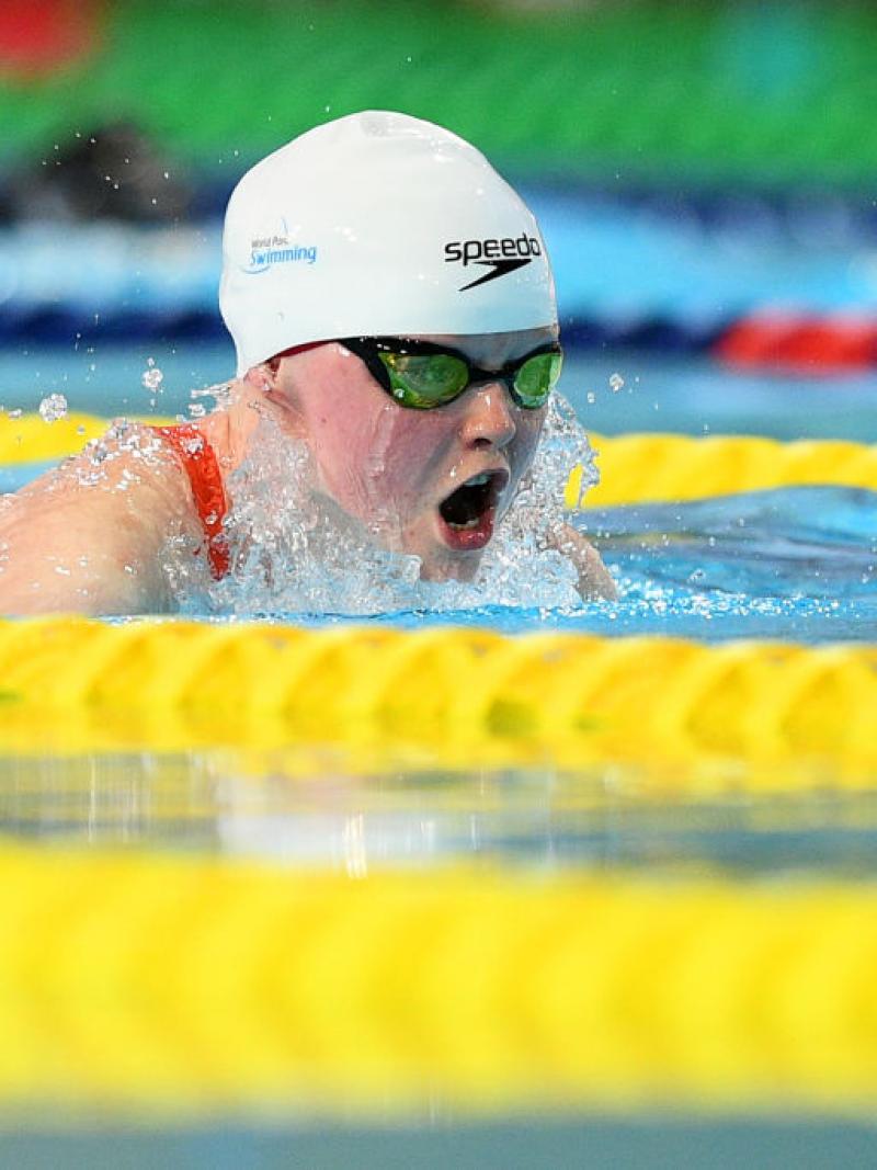 A female swimmer with a white cap swimming backstroke