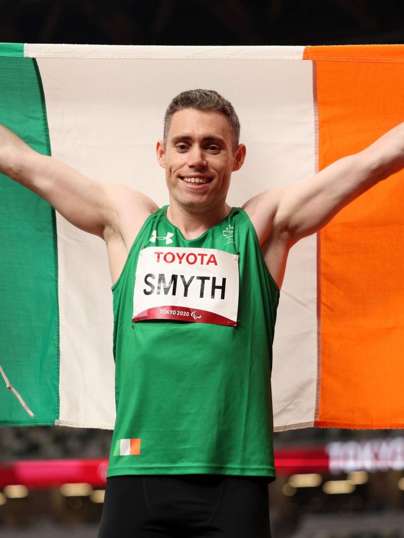 A male athlete holds up an Irish flag behind him as he celebrates a victory in the athletics stadium at Tokyo 2020.