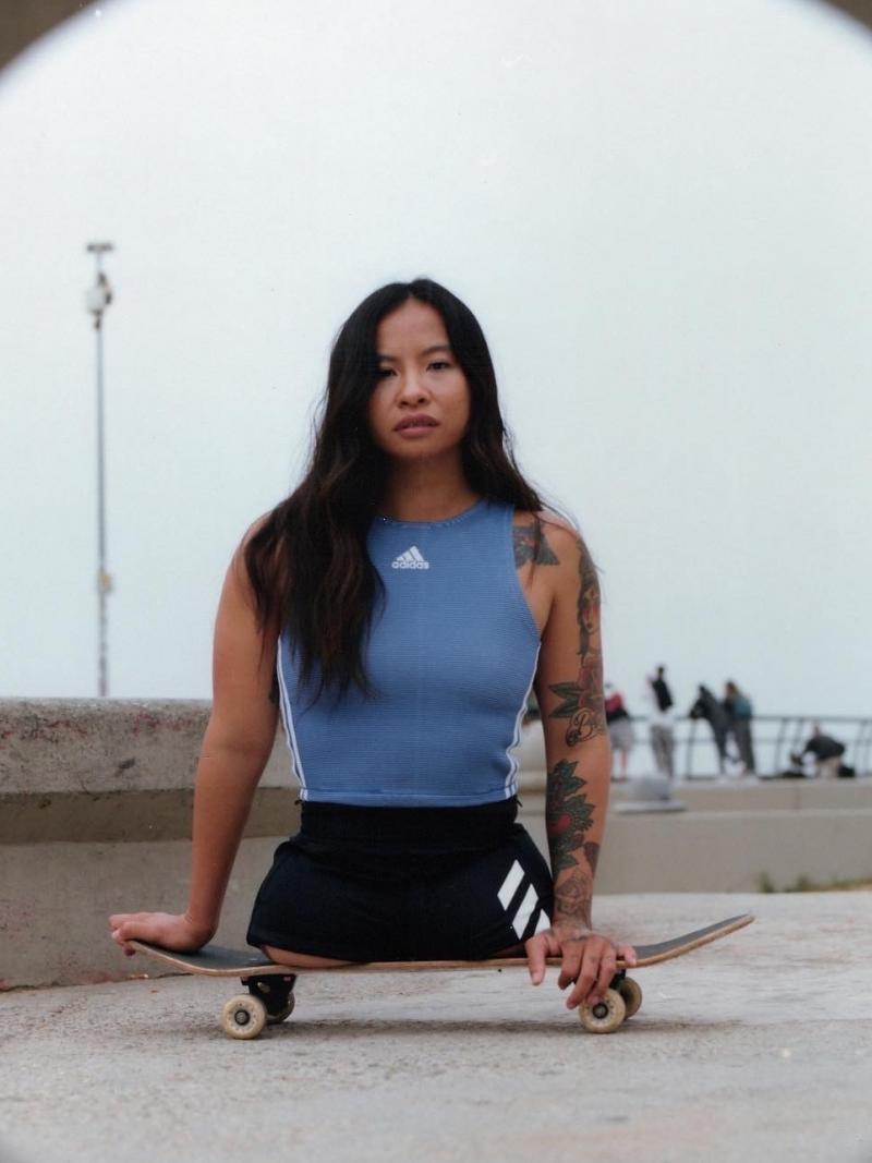 A young female without legs sits on a skateboard while wearing sports gear.